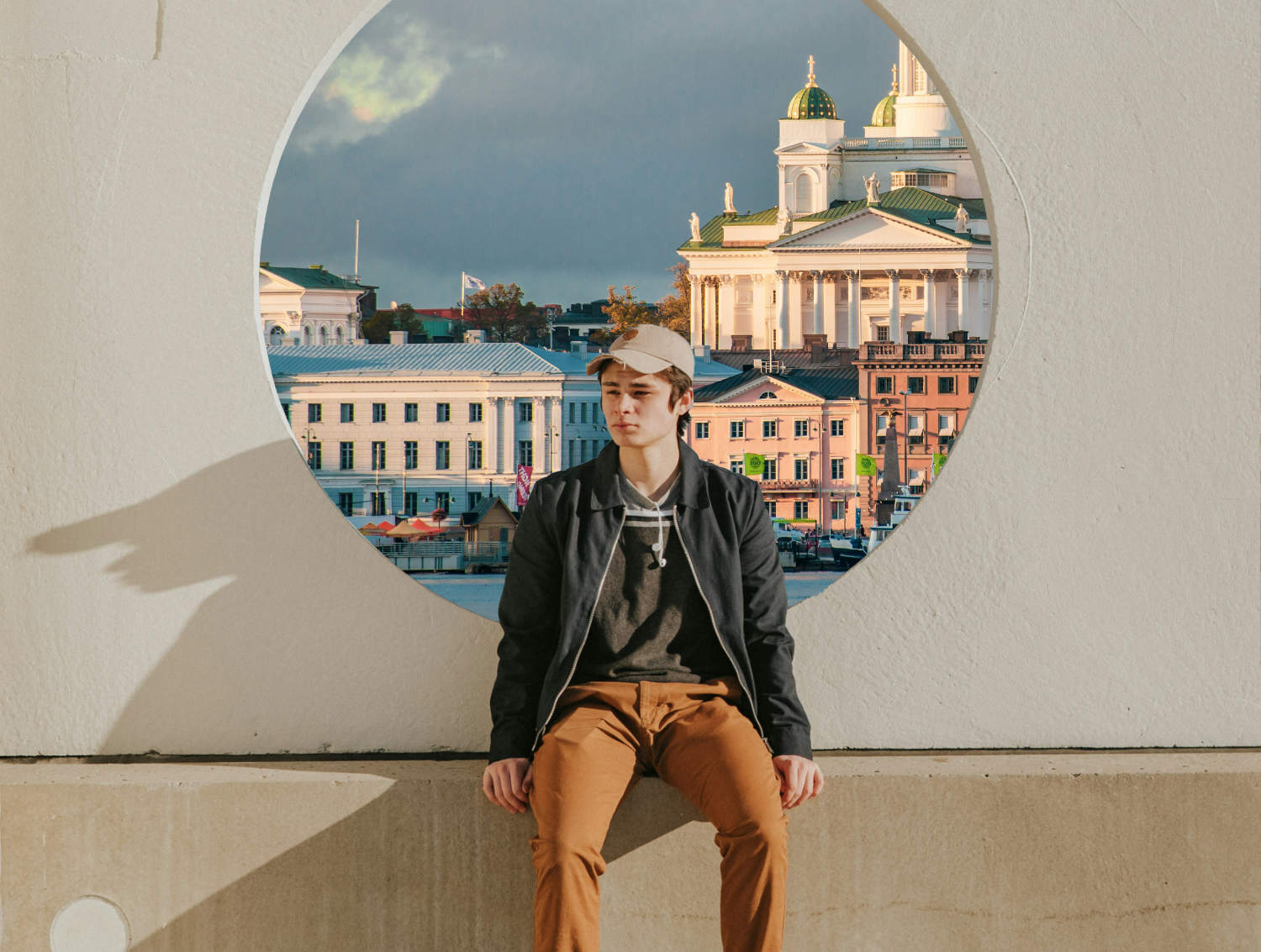 Teini istuu seinän vieressä. Ikkunassa takana näkyy Tuomiokirkko